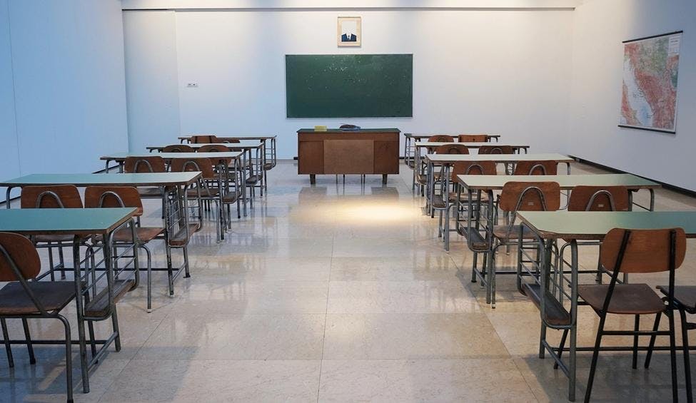 Et klasserom med pulter og stoler står i to rader rettet mot en tavle.