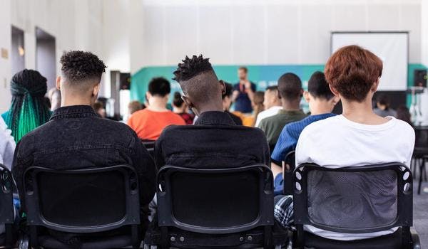 Tre ungdommer sitter bakerst i et klasserom og hører på en lærer snakke. 
