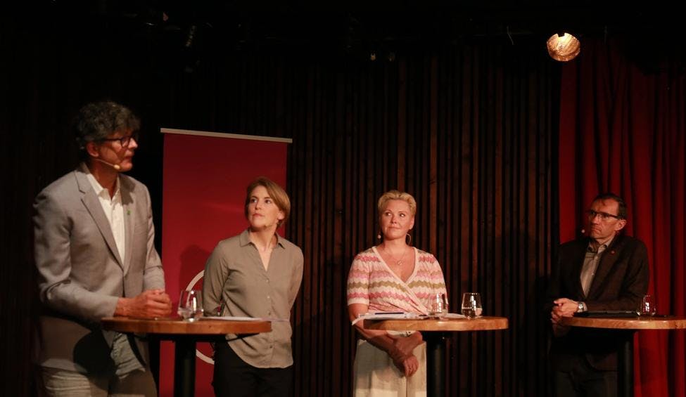 Fire politikere står foran rundbord på en scene imens de ser på hverandre. 