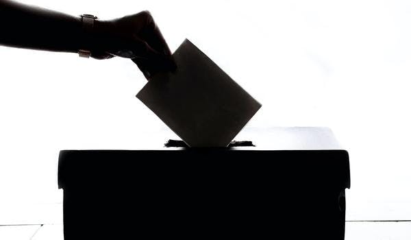 Et bilde i svart/hvitt av en hånd som legger en stemmeseddel i en boks